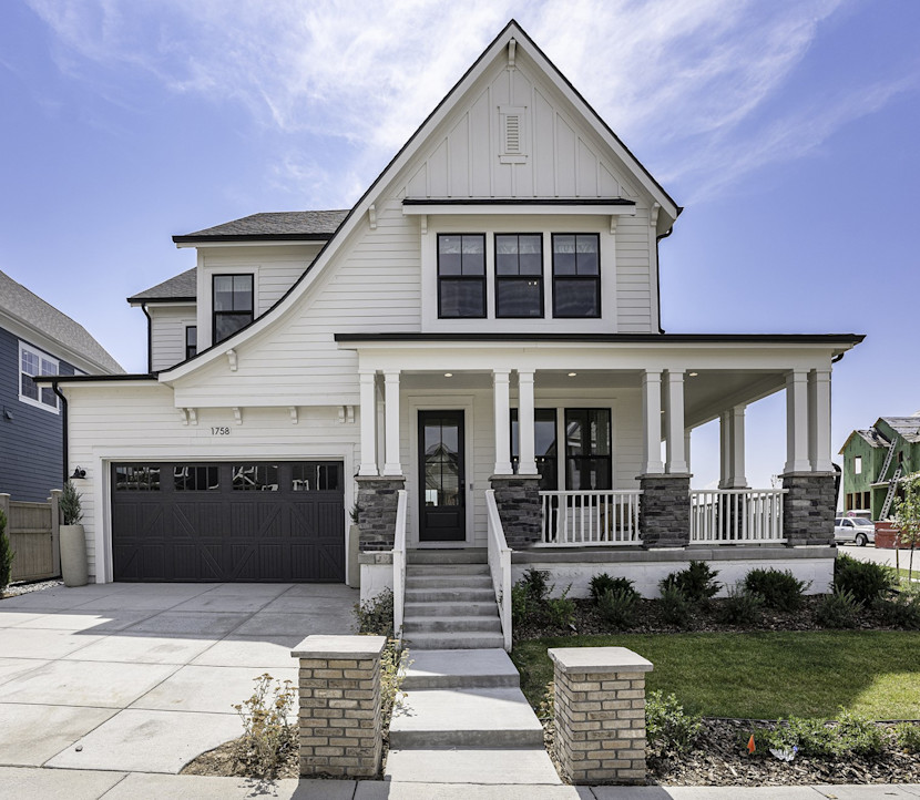 New construction home with peaked roof, double car garage, covered front porch, white siding and hedges.