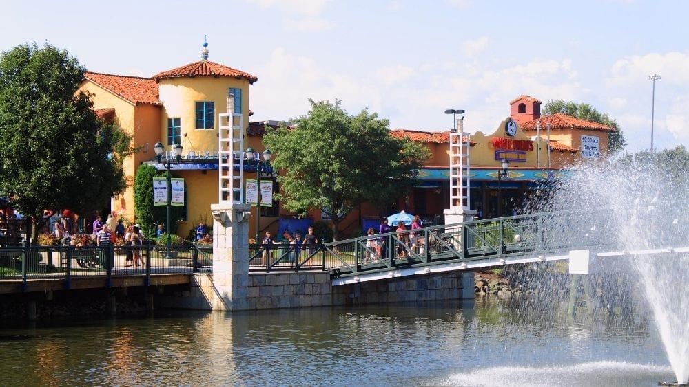 View of a large restaurant facing a river, with a bridge crossing the river and a fountain on the other side.