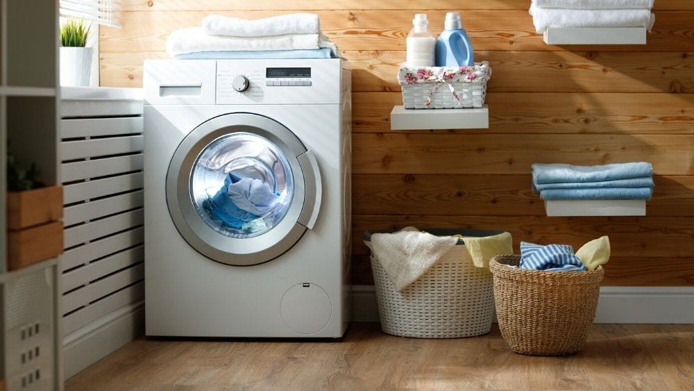 laundry room with a front-load washer, folding area, laundry baskets with clothes, shelves with folded towels and laundry soap.