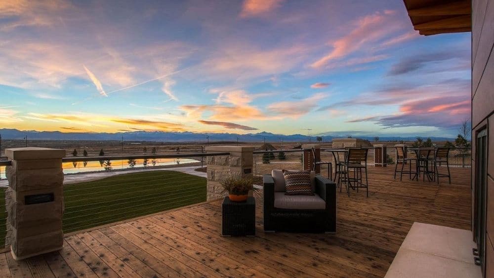 A wooden deck with comfortable chairs overlooking a lake at sunset.