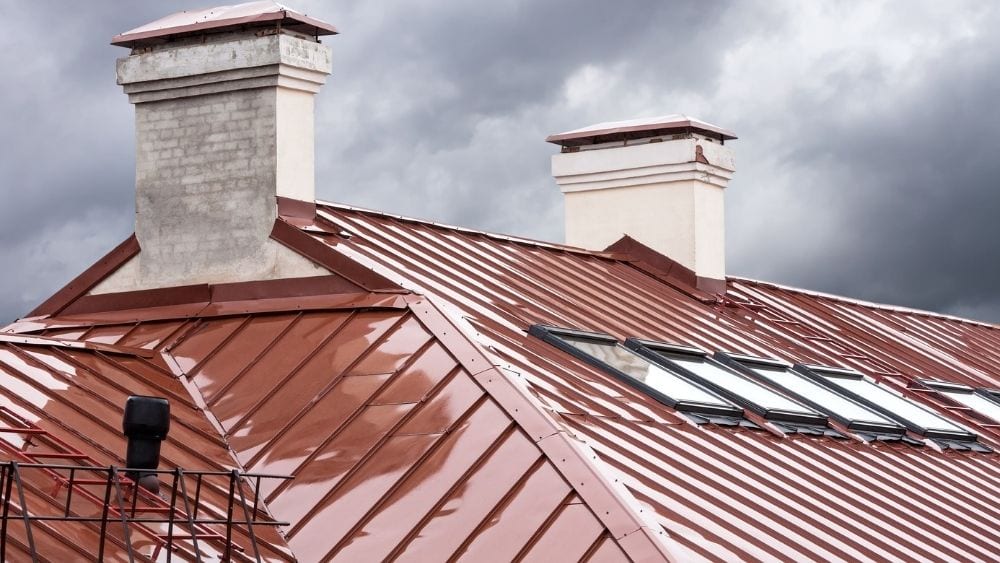 A red metal roof with two stone chimney stacks.