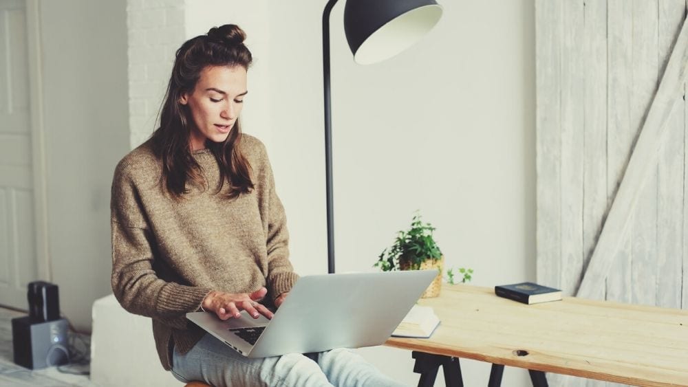 lady in a brown sweater with long brown hair sitting in front of a laptop