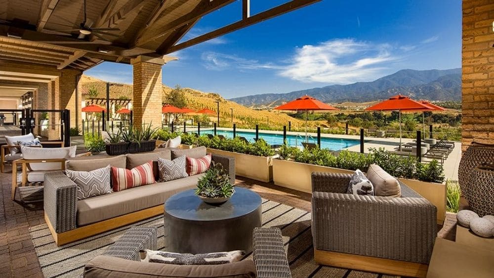 A furnished outdoor patio with an awning over the seating area and a public pool.