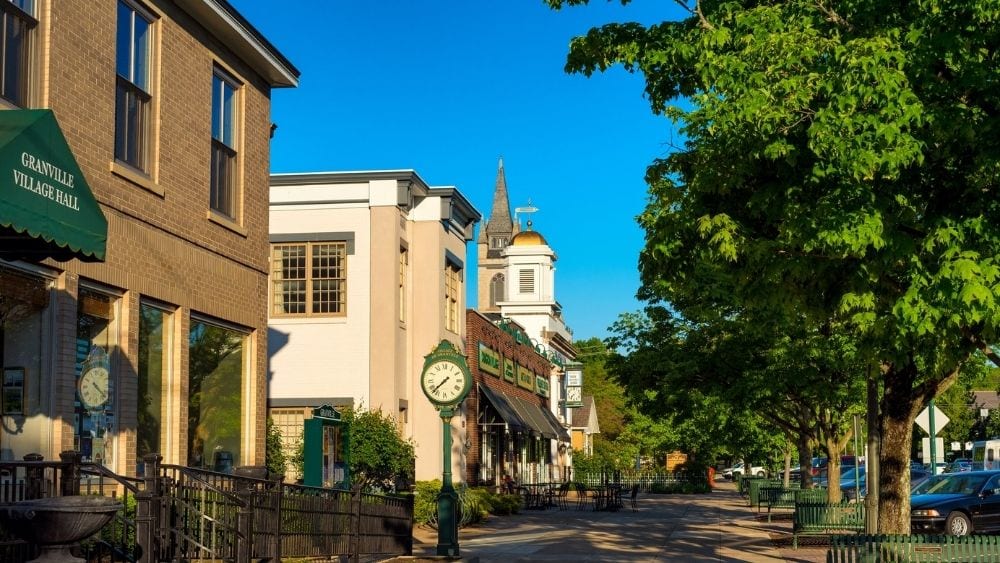 Angled view of a town square with white and beige buildings and green awnings.