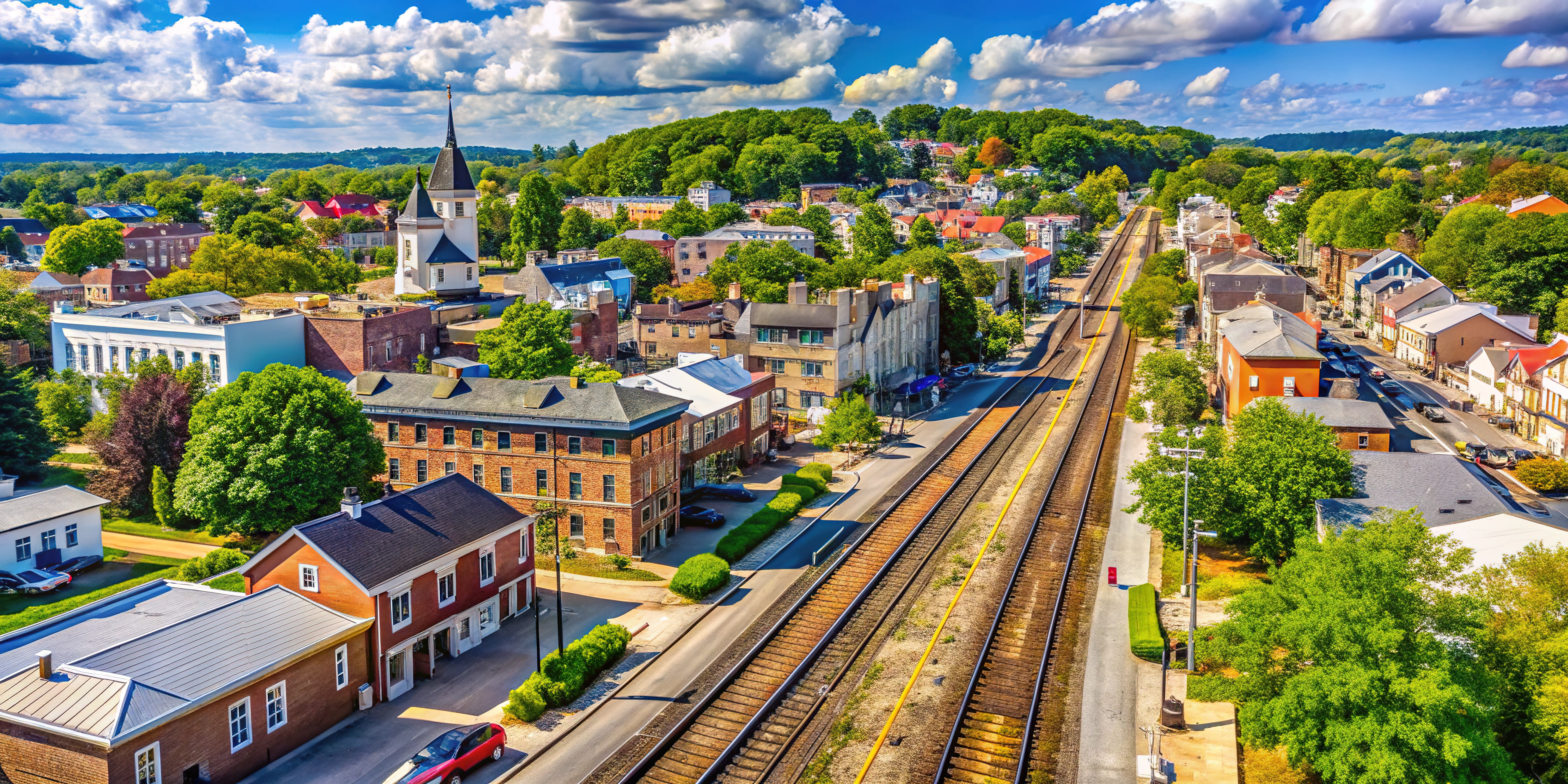 churches, buildings, train tracks bordered by trees and a blue sky