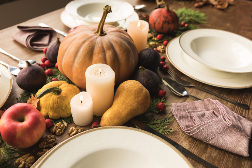 Table setting with pumpkin, gourds, candles, white dishes and cutlery on a wooden table