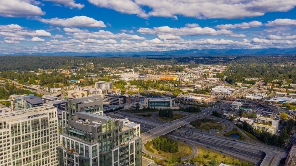Aerial view of a city and roadways with lots of greenery and a blue sky.