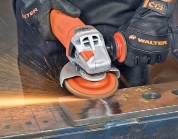 Orange angle grinder in action with sparks flying, used by a worker wearing WALTER protective gloves, grinding a piece of metal on a work surface.