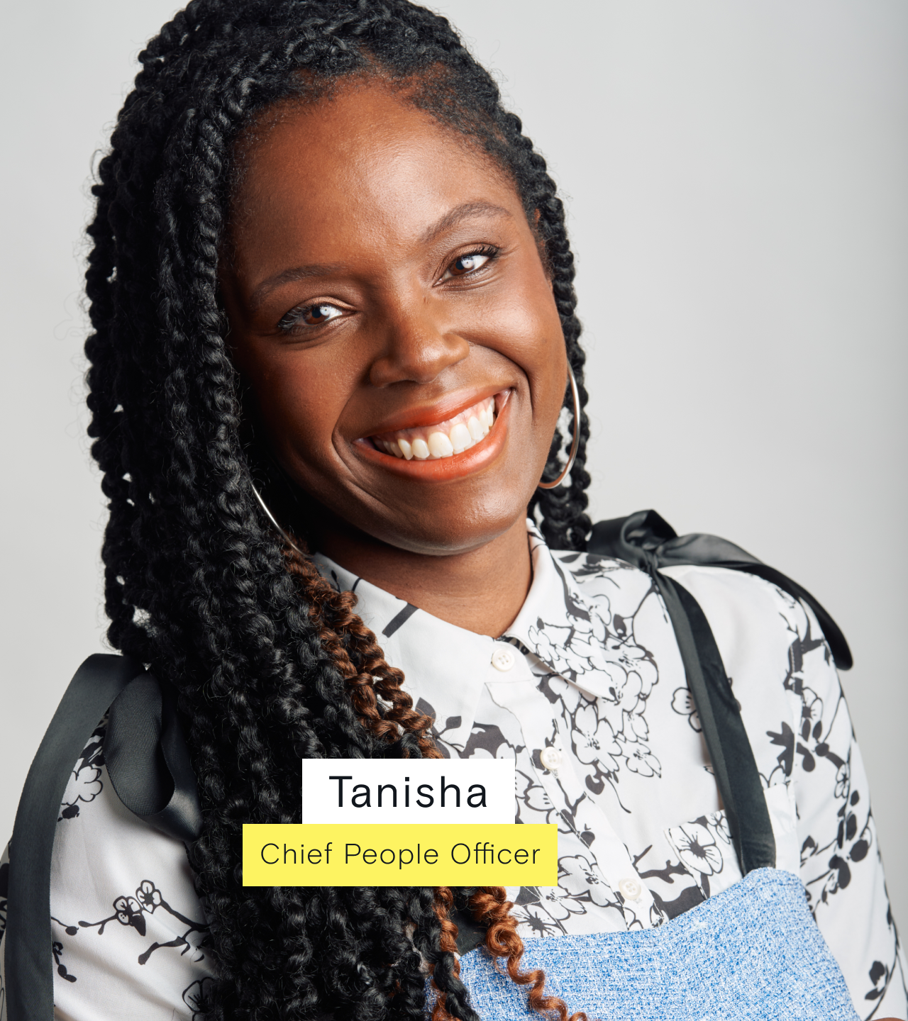 EZRA's chief people officer wearing a white shirt with black details and denim overalls, smiling at the camera.
