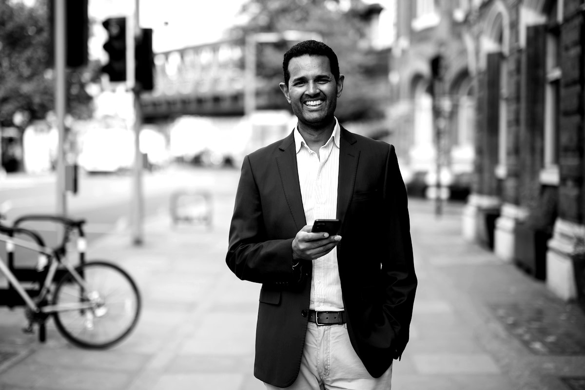 Black and white photograph of a smiling man in a suit holding his cellphone.