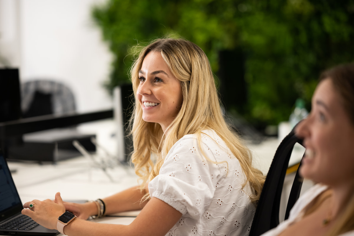 A woman in a white blouse sat at her desk, smiling up at someone.