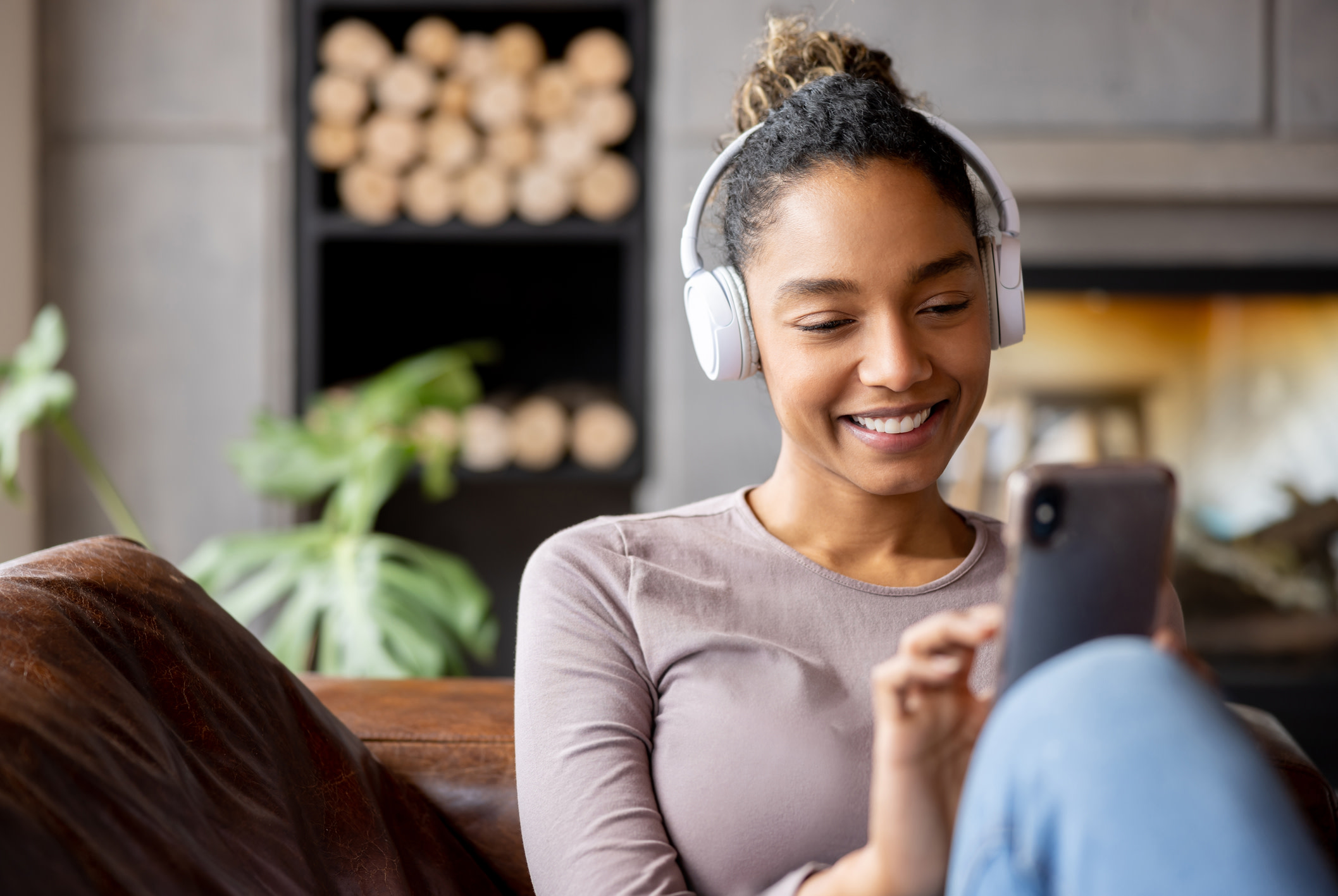 Happy woman relaxing at home using headphones while looking at social media on her cell phone and smiling