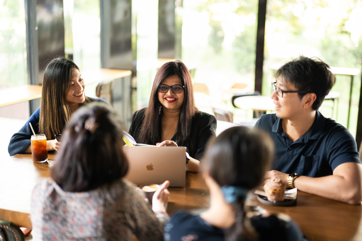 Five colleagues sat around a table with a laptop, discussing work.