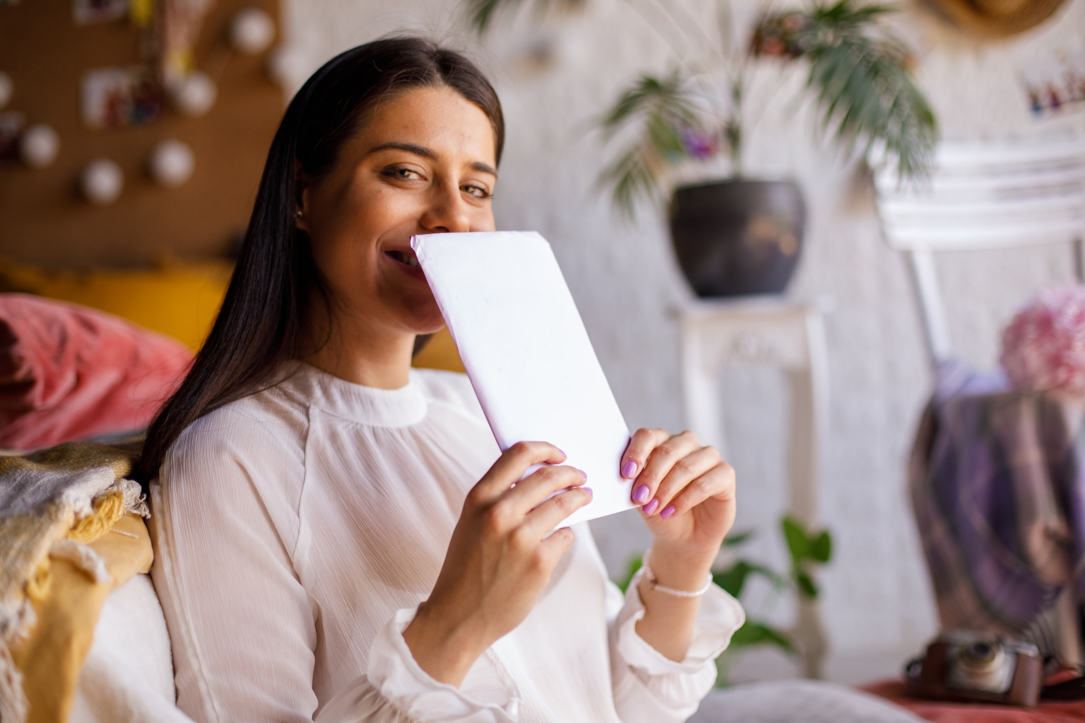 Copy space shot of cheerful young woman hiding her smile behind a love letter from a crush while looking at camera