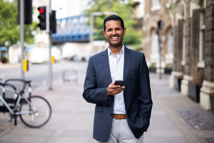 Man wearing a suit on the pavement smiling with his phone in his hand