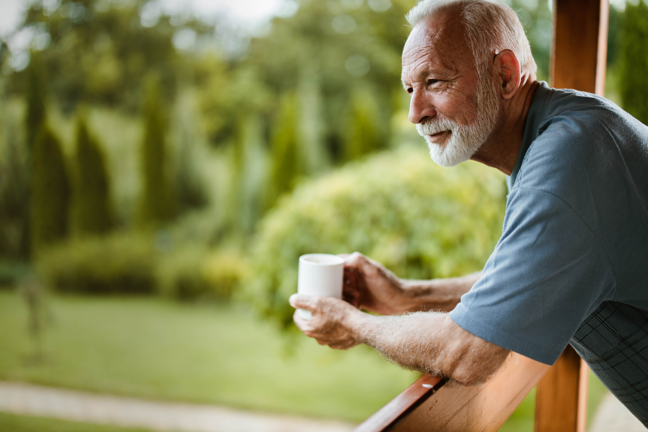 Senior man having his morning coffee on a balcony and day dreaming. 

