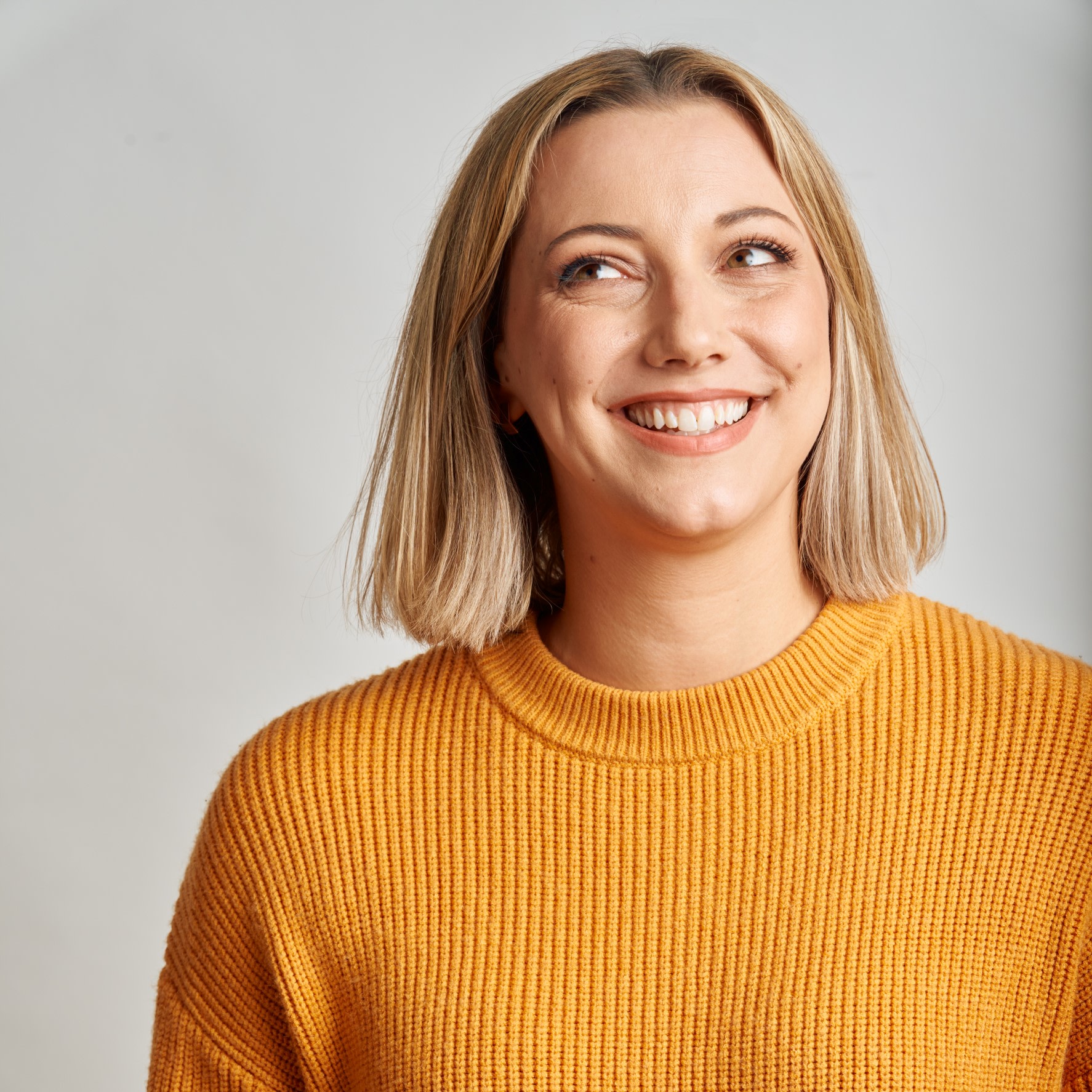 Smiling woman in orange knitted top, looking up to the left
