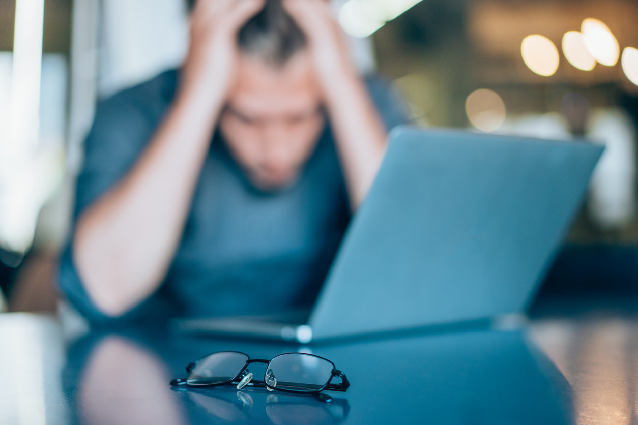 Out of focus man with head in hands, pair of glasses in foreground