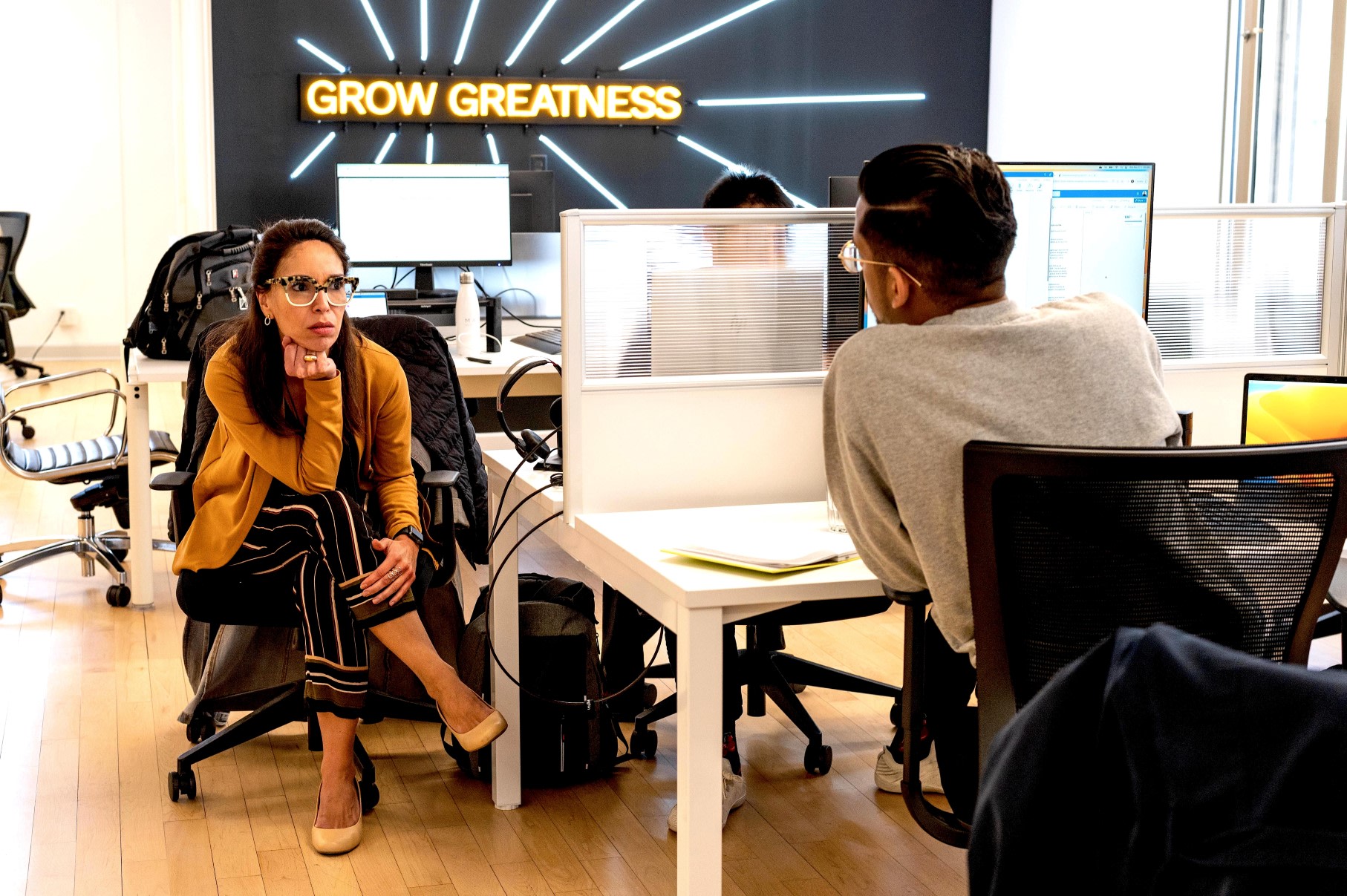 Zwei Kollegen diskutieren im EZRA-Büro, hinter ihnen ein Neonschild mit der Aufschrift 'Grow Greatness'