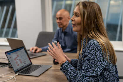 A woman is leading a meeting, sat at a meeting table in a meeting room.