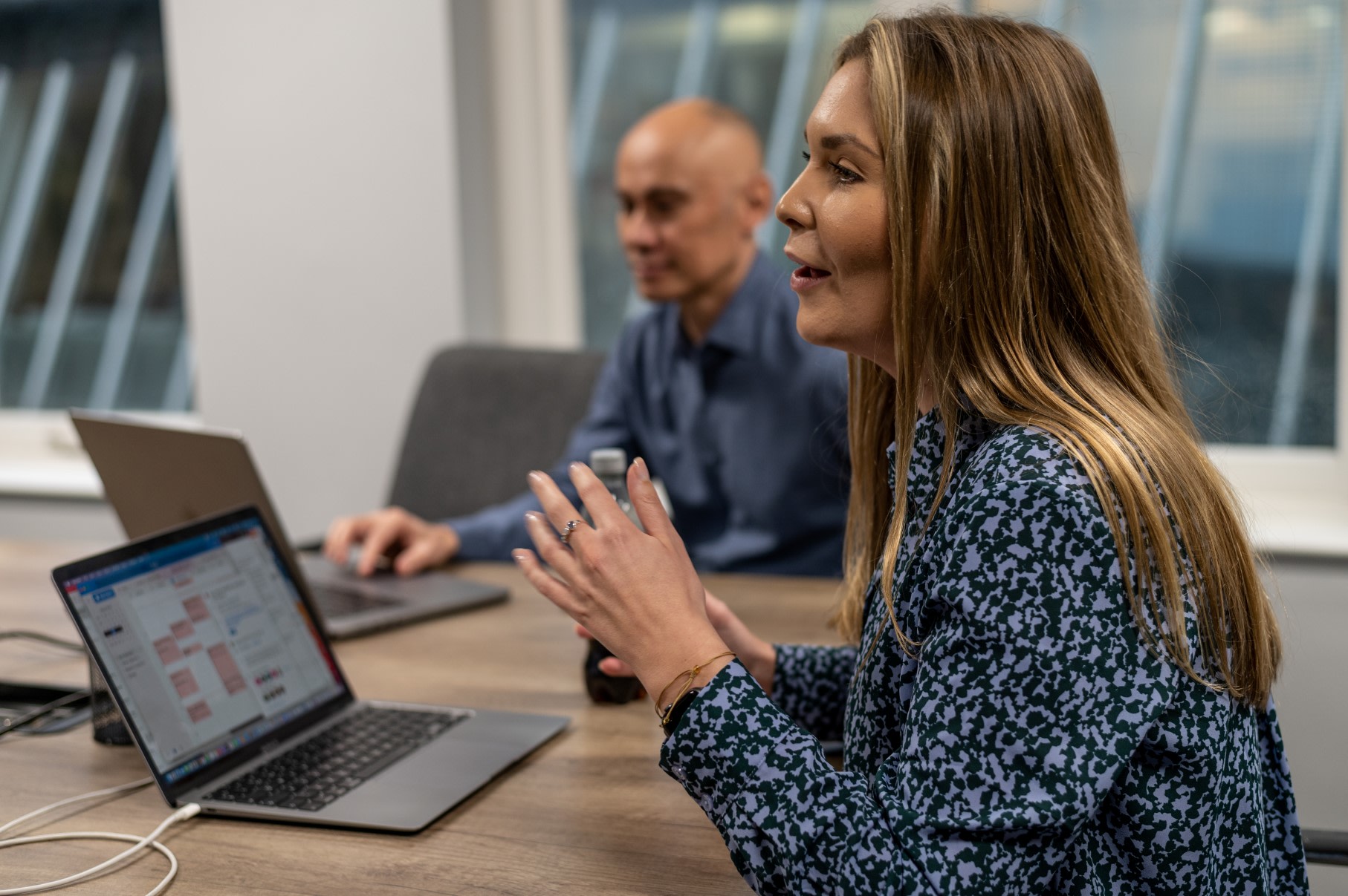A woman is leading a meeting, sat at a meeting table in a meeting room.