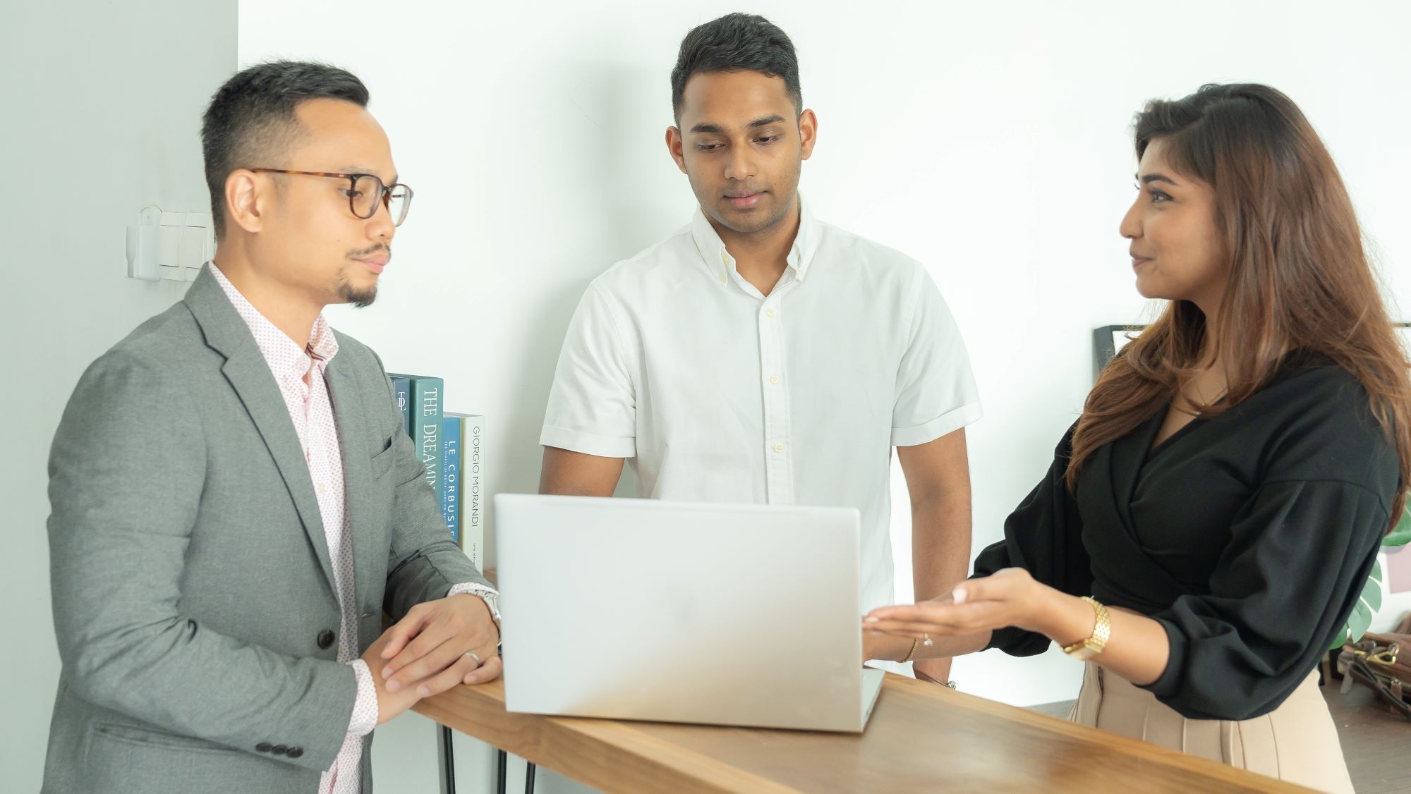 Three people have a discussion around a laptop.