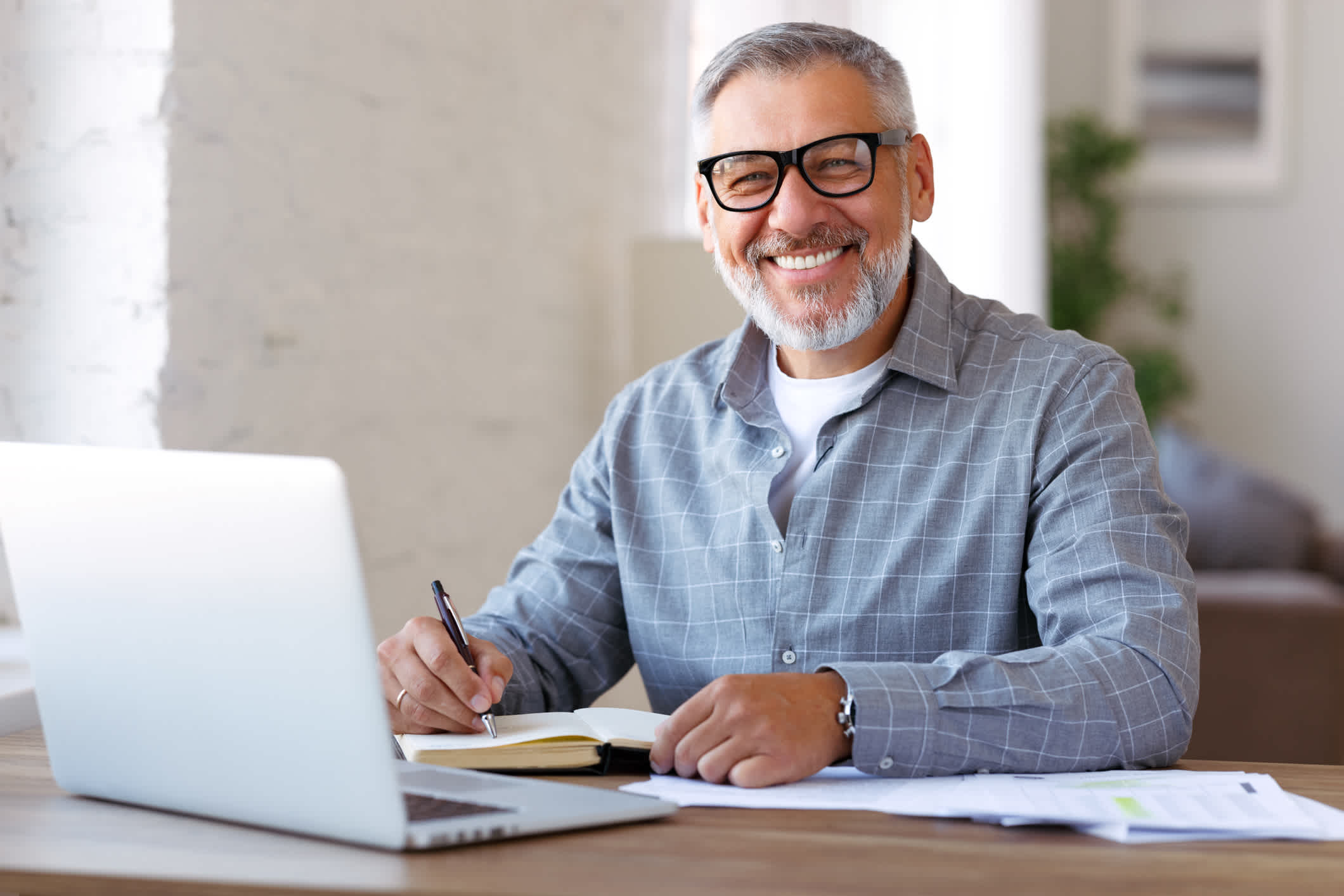 Handsome positive senior man wearing glasses enjoying distant education while sitting at his cozy workplace with laptop computer at home, retired pensioner learning studying online indoors