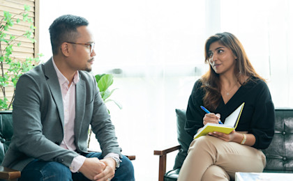 Woman sat with a notepad and pen speaking to a man who is listening intently.