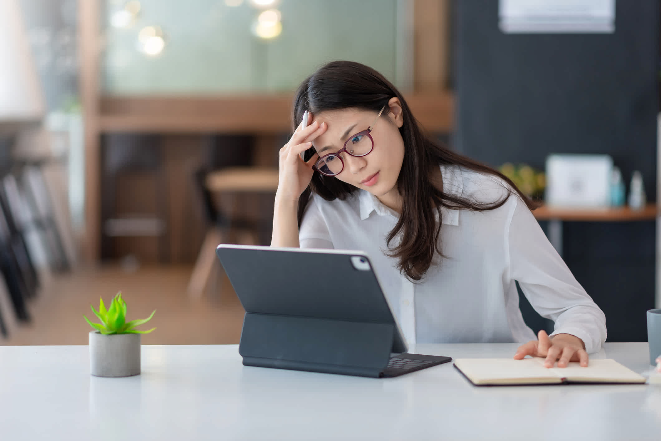 Image of an Asian woman who is tired and overthinking from working with a tablet at the office.

