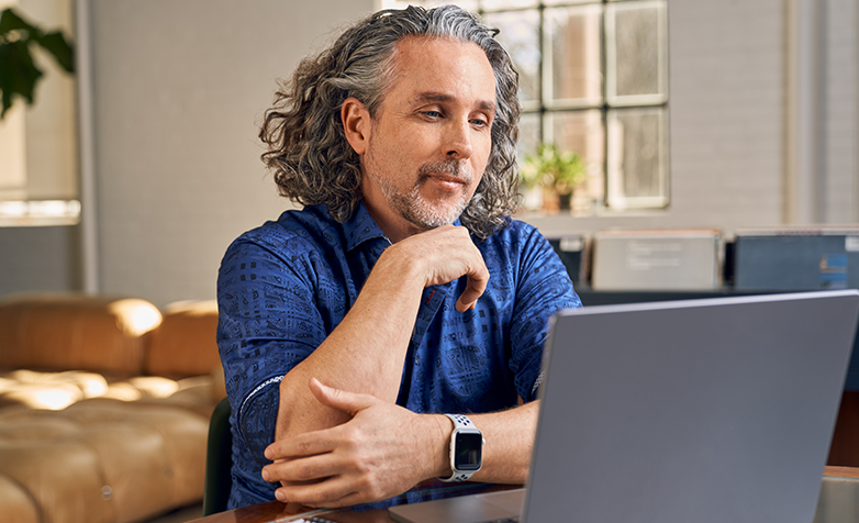 A middle-aged man smiling looking at his laptop.