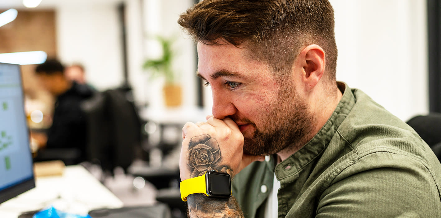 Unshaven man with rose tattoo on hand, wearing a green shirt, facing a stressful situation at work