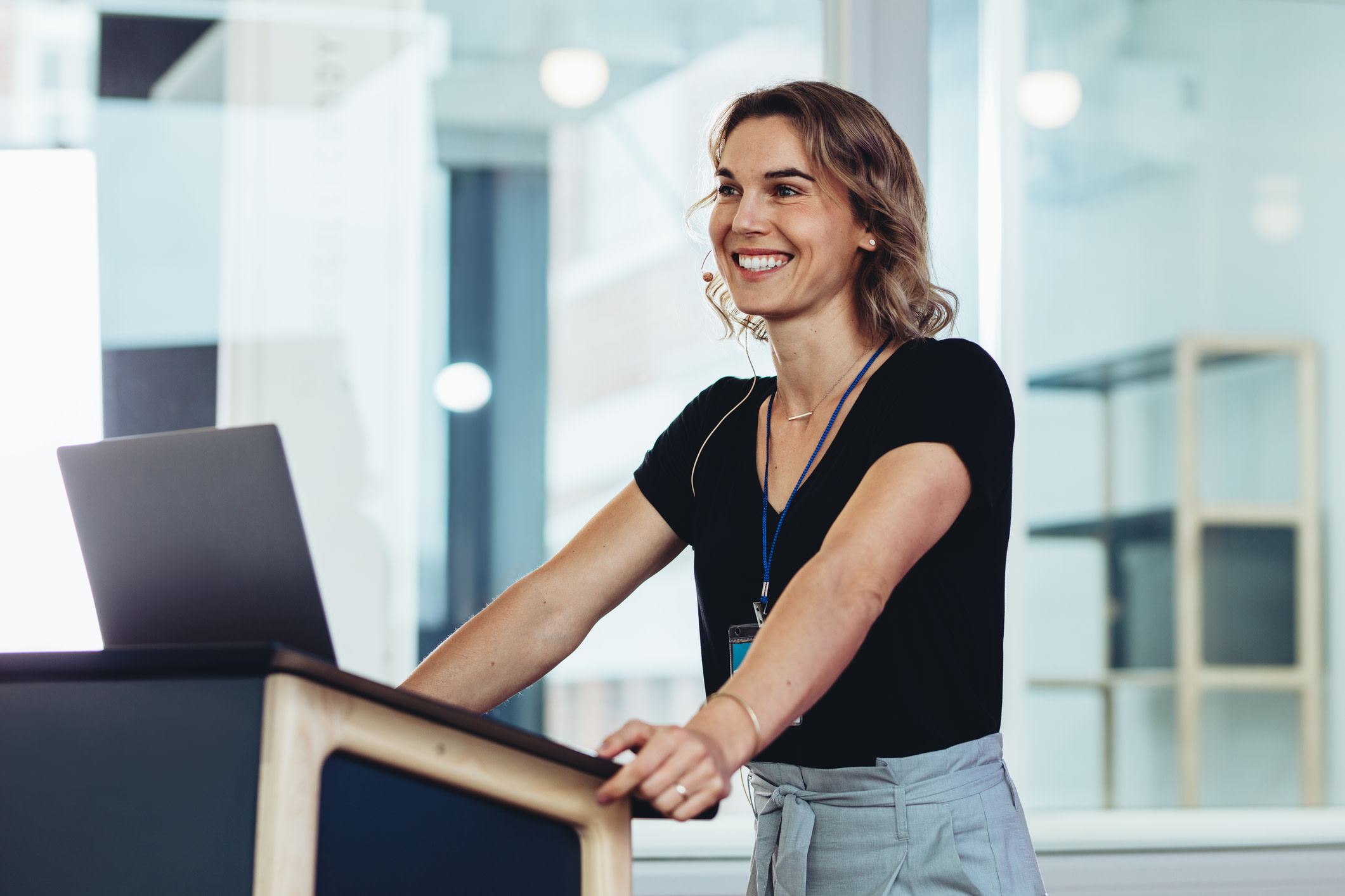 Businesswoman standing at podium with laptop and smiling. Successful female business professional addressing a conference.