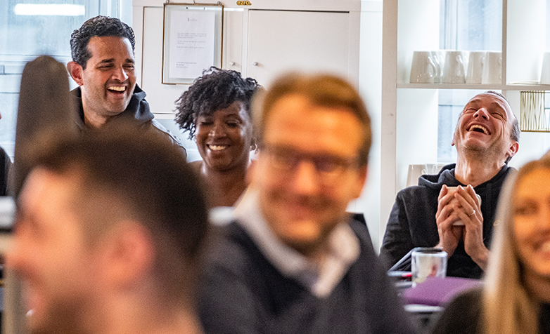 A woman sitting on a sofa, smiling and waving looking at her phone.