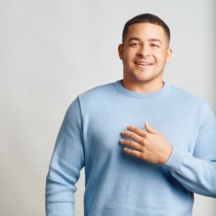 Man smiling and looking into camera with his hand on his chest 