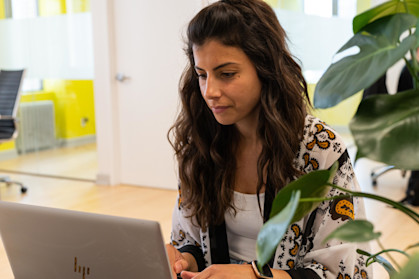 Woman sat in an office at her desk, working at a silver laptop.