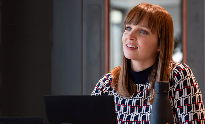 Donna indossa un maglione azzurro, bianco e rosso a motivi, ascoltando attentamente il coaching sul cambiamento e la trasformazione.