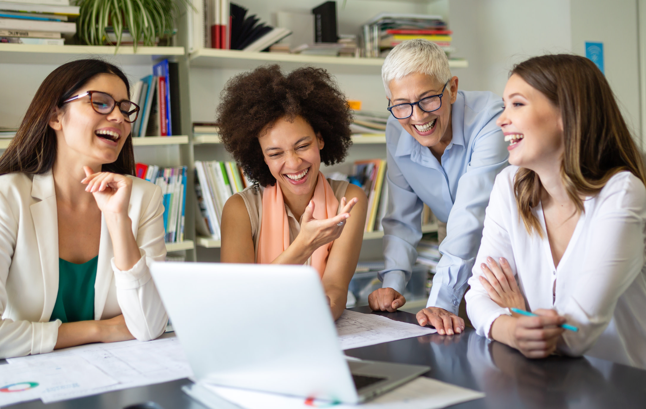 Four colleagues sat around a laptop, working and laughing together in an office.