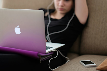 Woman with her headphones in, lounging on a sofa and pretending to work at her laptop.