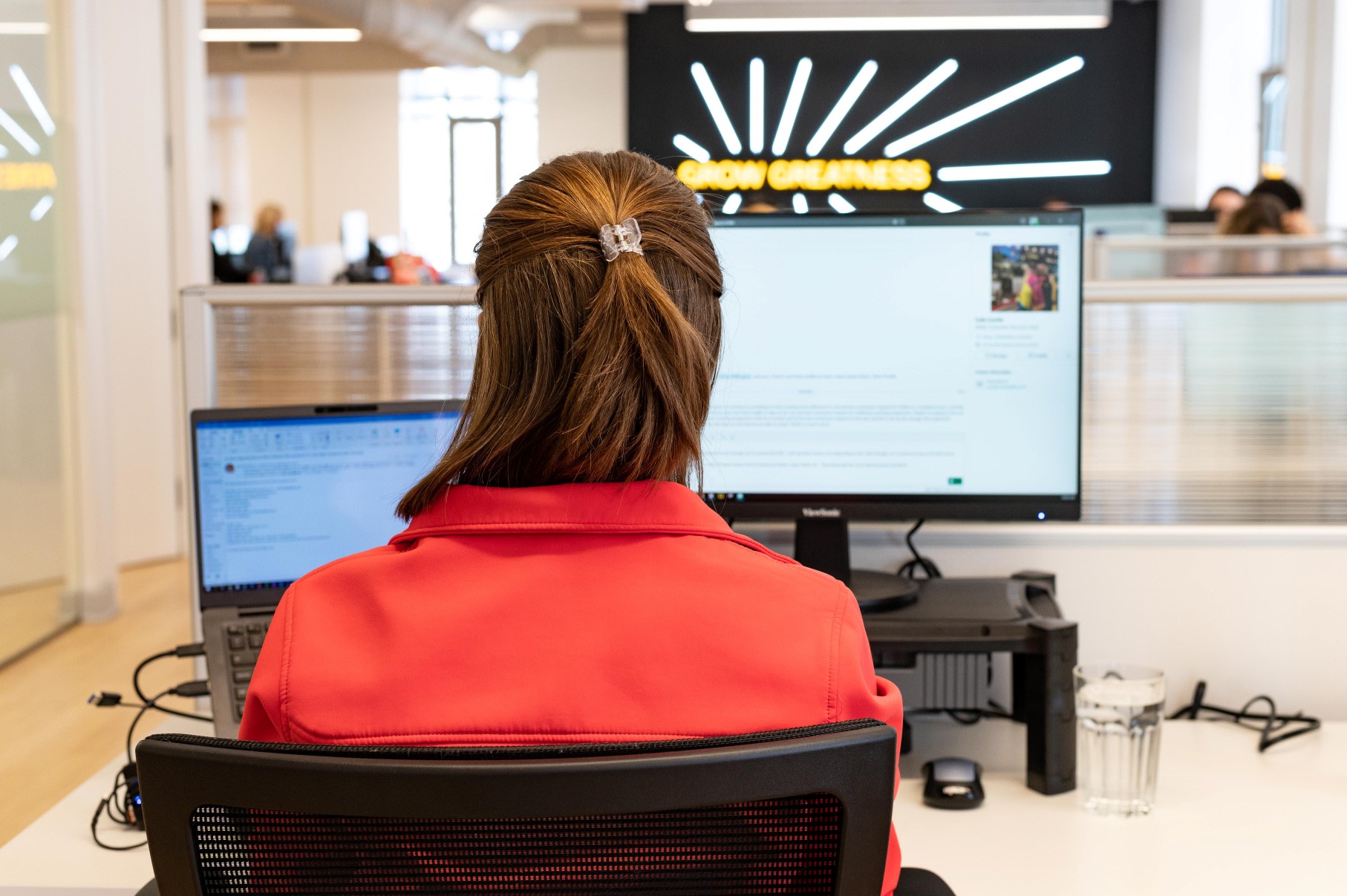 Back of a woman with brunette hair, while she works on a desktop computer in the EZRA office