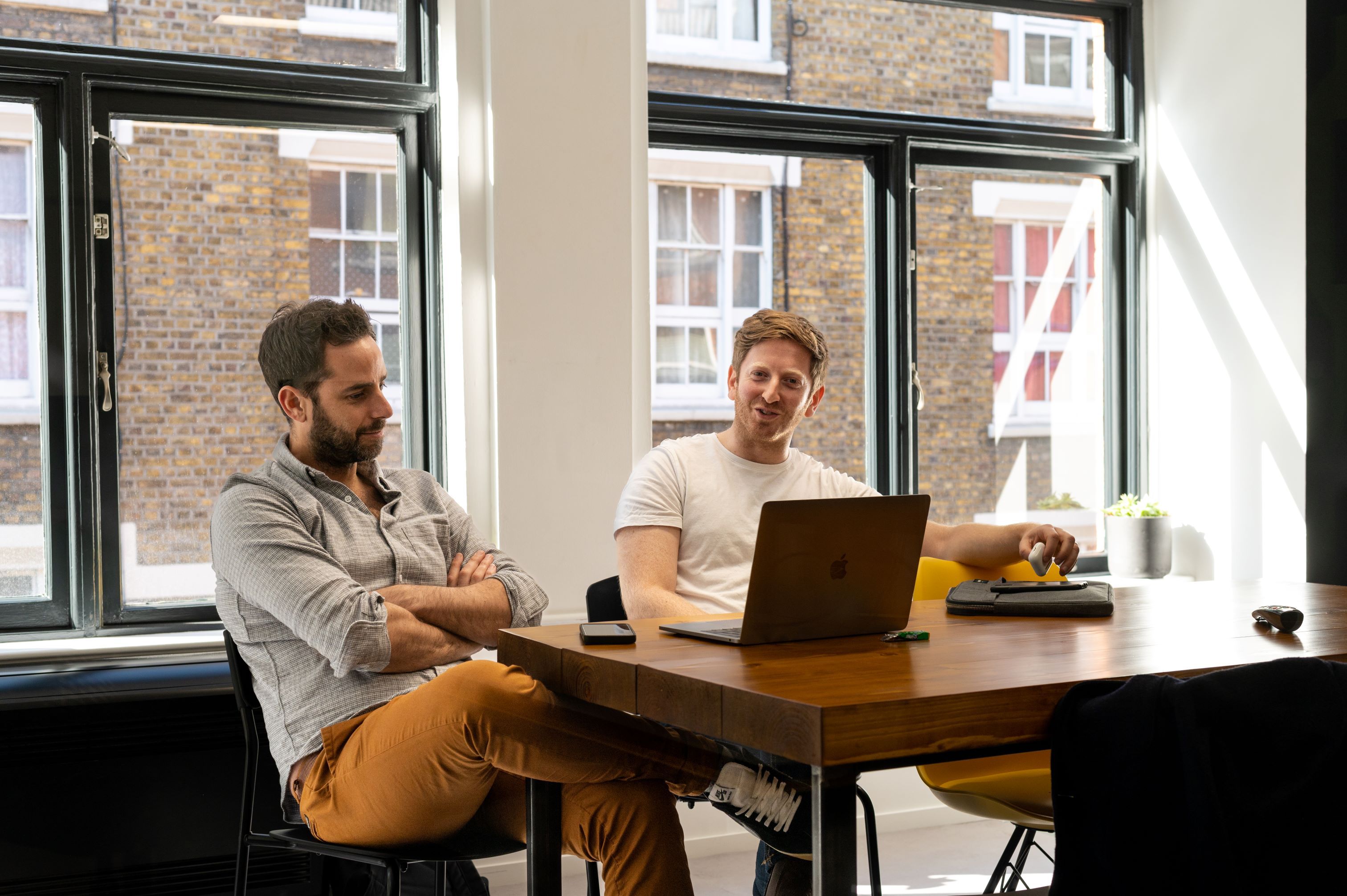 Two men sitting at a desk with a laptop between them