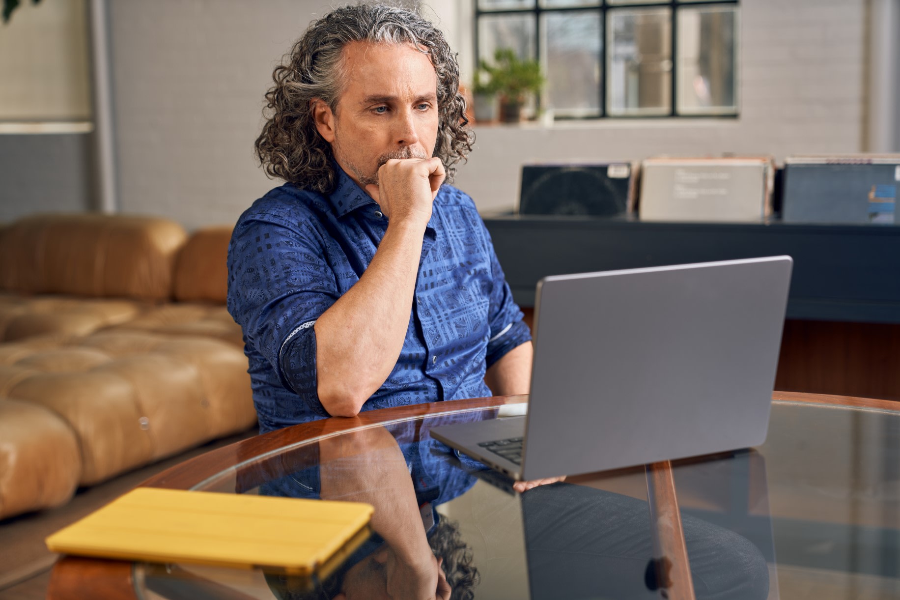 Man in dark blue shirt, looking at laptop screen whilst resting clenched fist against his mouth
