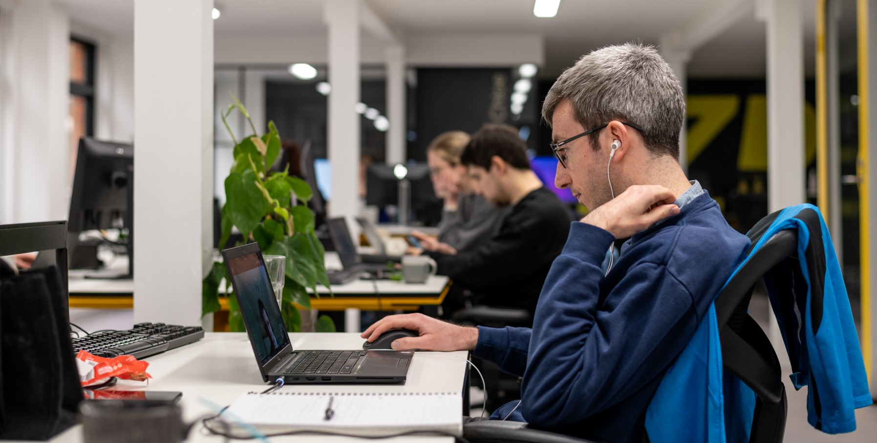 Man sat on a video call at his laptop in the office with his headphones in.