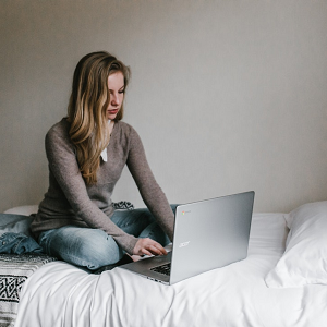 Image of female student sitting on bed using laptop.