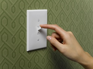 a woman's hand switches a white light on a green wallpapered wall