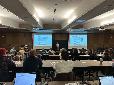 A conference room full of tabletops school-room style looking at an a/v presentation at the front of the room.