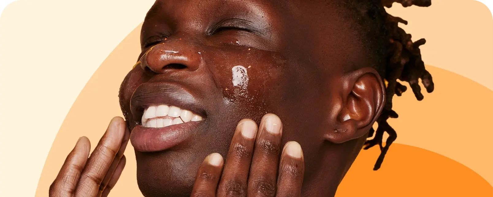 A person smiles with eyes closed, applying a glossy skincare product on their face, using their hands. The background features a gradient of light to dark orange hues.
