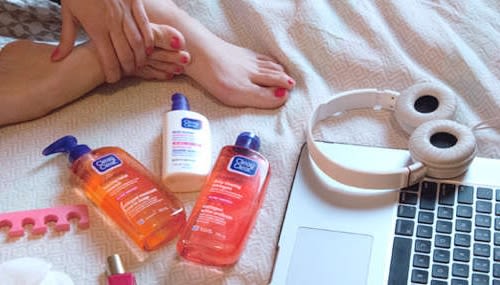 Three Clean & Clear® product bottles next to a laptop and a headphone in bed.