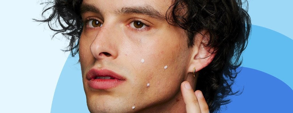 A person with curly hair is applying small white dots on their cheek. The earlobe has a gold hoop earring. The background features blue gradient curves.