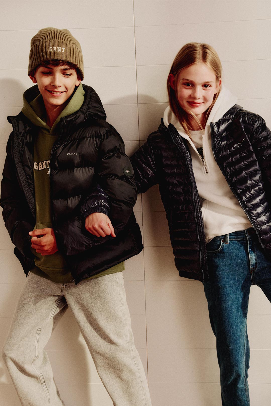 Two children wearing Gant puffer jackets with casual layers, standing against a light wall.