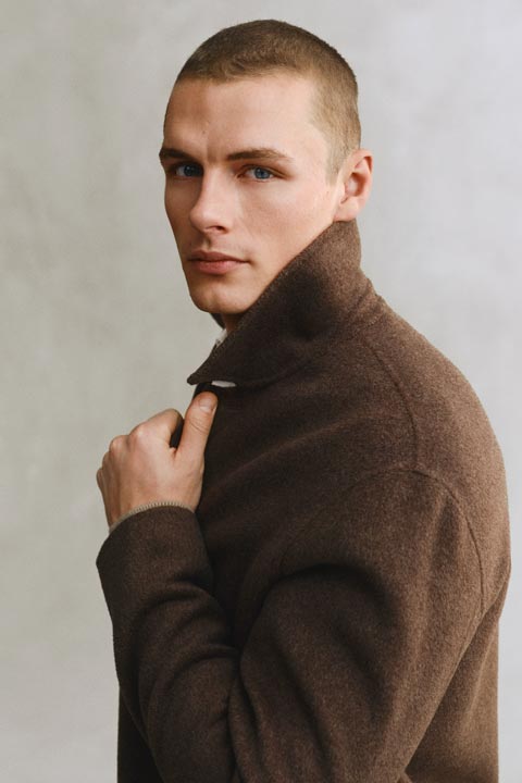 Model styled in a GANT brown wool coat, sidefacing with collar raised against a neutral background.